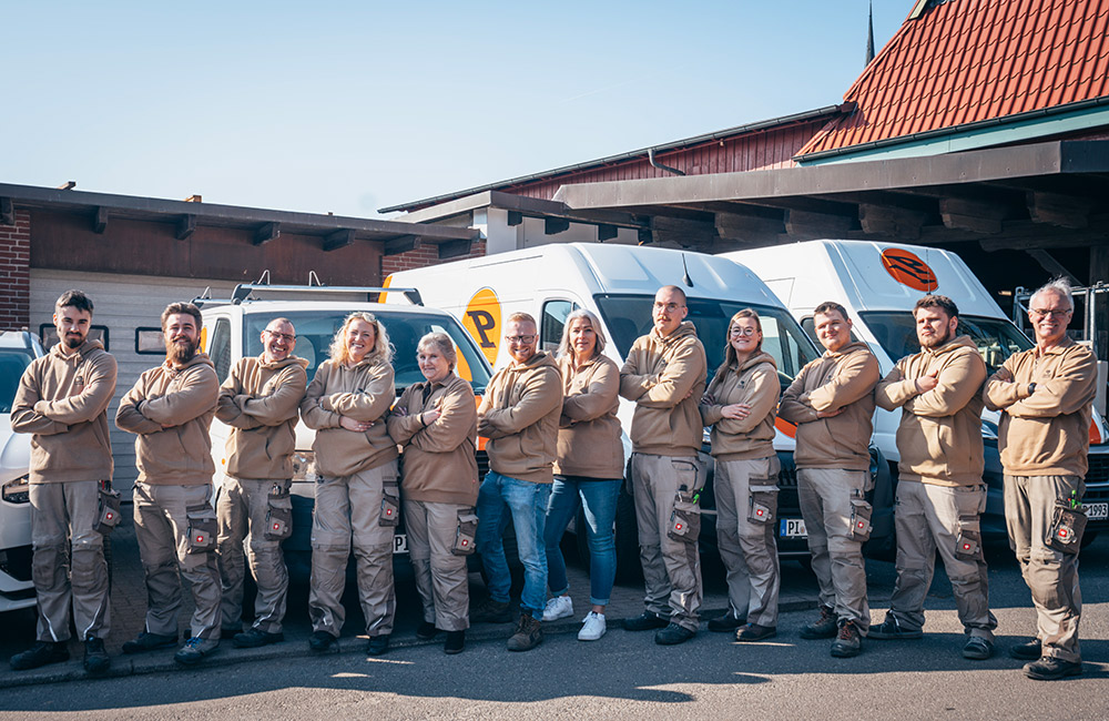 Eine Gruppe von Menschen in beigefarbener Arbeitskleidung steht selbstbewusst vor weißen Transportern