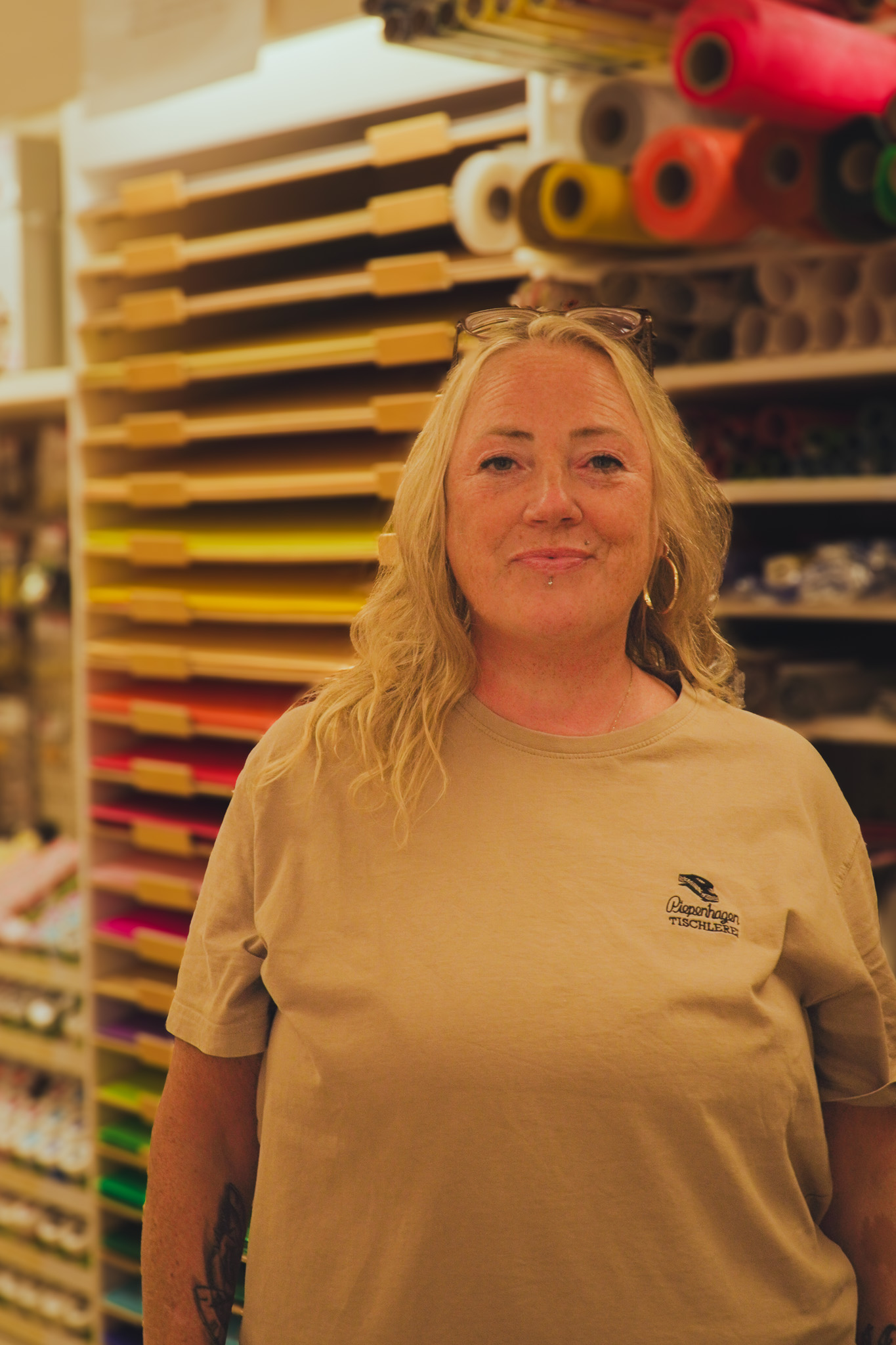 Laechelnde blonde Frau im beigen Shirt vor buntem Papierregal im Laden