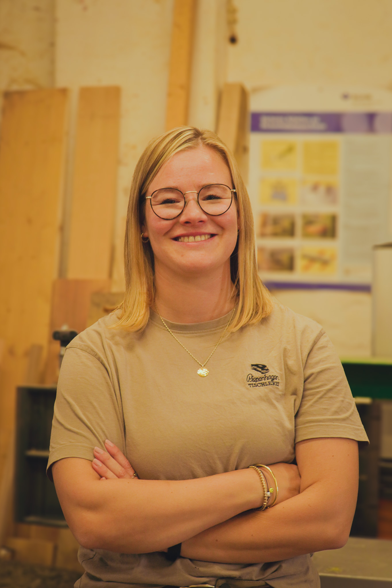 Laechelnde blonde Frau mit Brille und beigem Shirt in einer Tischlerei